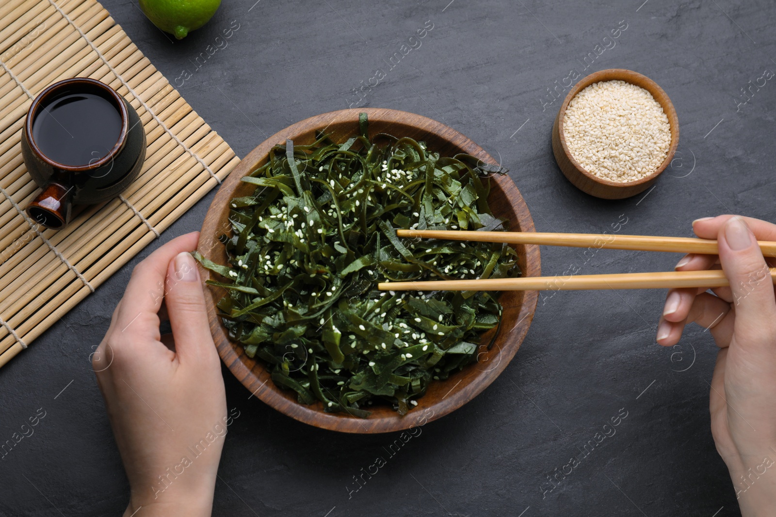 Photo of Woman eating fresh laminaria (kelp) seaweed at black table, top view