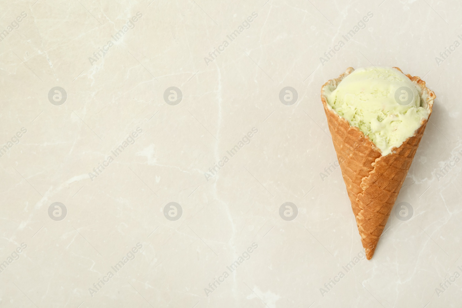 Photo of Delicious green ice cream in wafer cone on light marble table, top view. Space for text