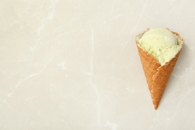 Delicious green ice cream in wafer cone on light marble table, top view. Space for text