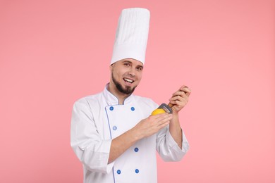 Photo of Happy professional confectioner in uniform holding grater and lemon on pink background