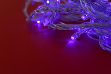 Photo of Glowing Christmas lights on burgundy background, space for text