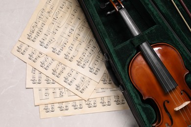 Photo of Violin, bow in case and music sheets on light grey table, top view