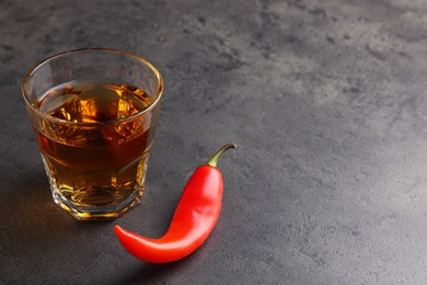 Photo of Red hot chili pepper and vodka in glass on grey table, space for text