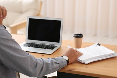 Man working with documents at wooden table in office, closeup