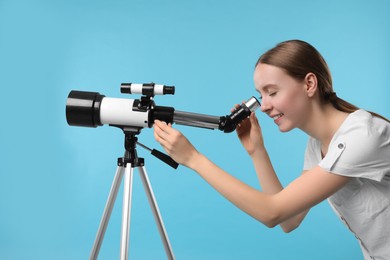 Photo of Young astronomer looking at stars through telescope on light blue background
