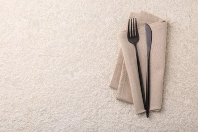 Photo of Stylish cutlery and dinner napkin on beige textured table, top view. Space for text