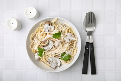 Photo of Delicious pasta with mushrooms served on white tiled table, flat lay