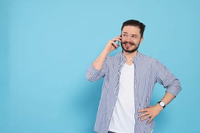 Photo of Happy man talking on smartphone against light blue background. Space for text