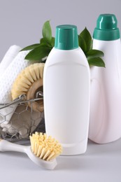 Bottles of cleaning product, brushes, rags and floral decor on light background