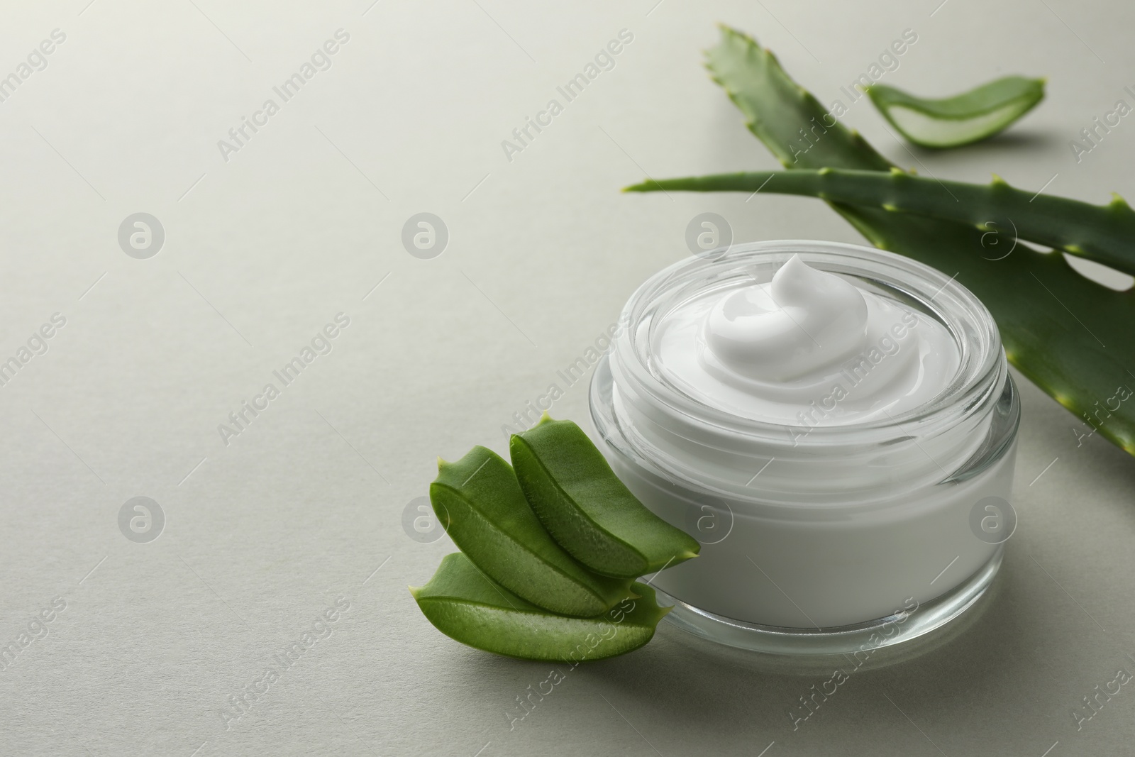 Photo of Jar with cream and cut aloe leaves on light grey background, closeup. Space for text