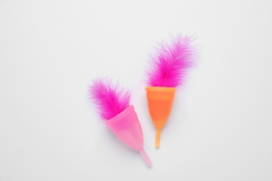 Photo of Menstrual cups with pink feathers on white background, flat lay