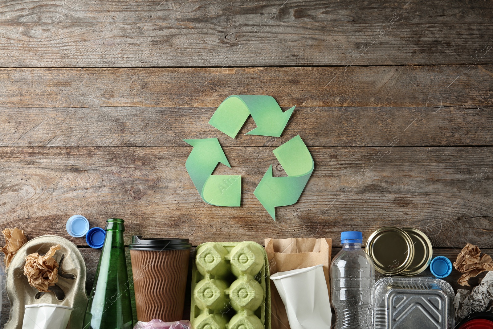 Photo of Recycling symbol and different garbage on wooden background, top view