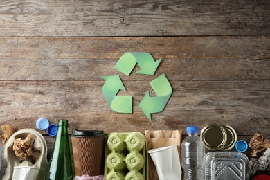 Photo of Recycling symbol and different garbage on wooden background, top view