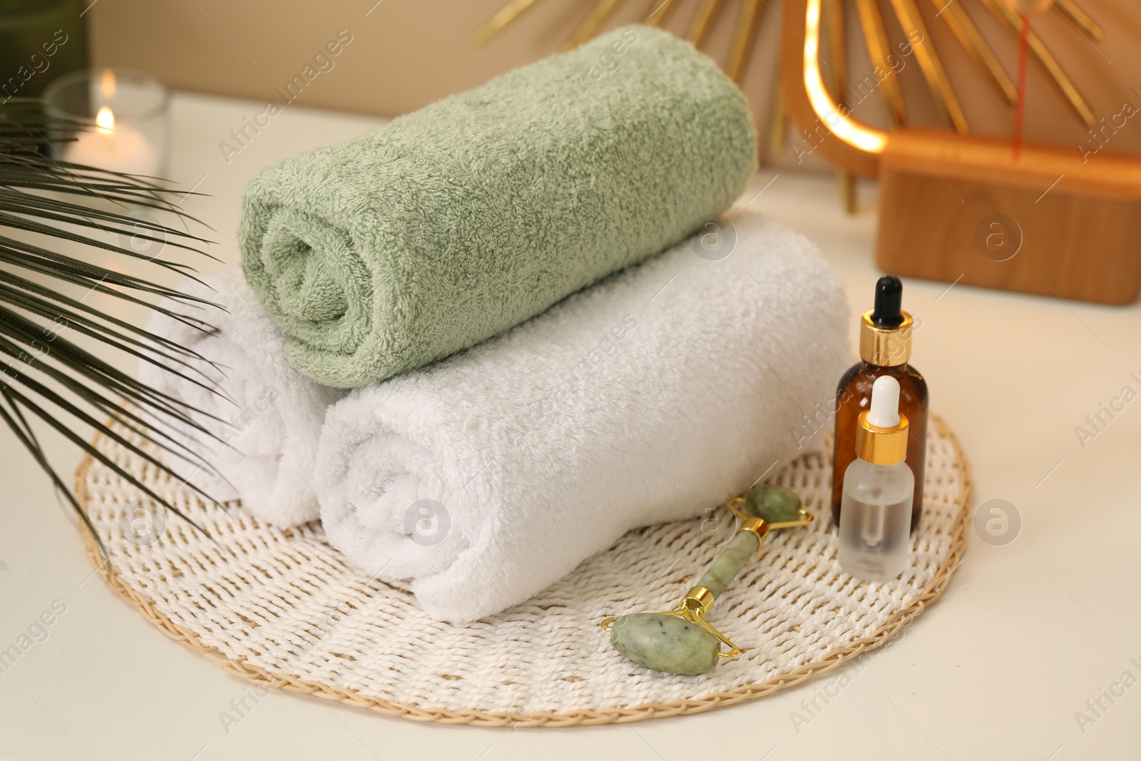 Photo of Spa composition. Rolled towels, cosmetic products and face roller on table