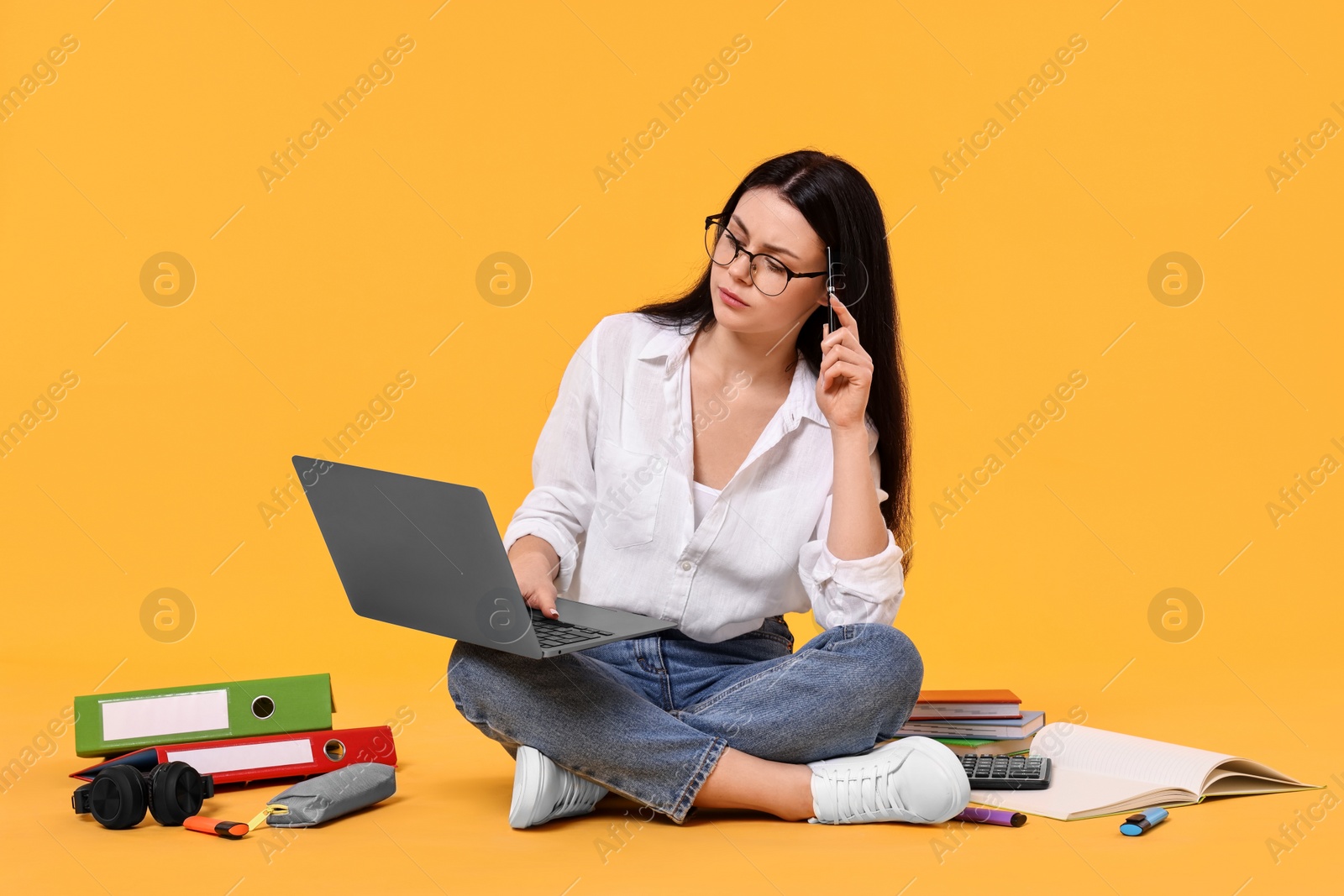 Photo of Student with laptop sitting among books and stationery on yellow background