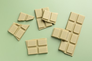 Photo of Pieces of tasty matcha chocolate bars on light green background, top view