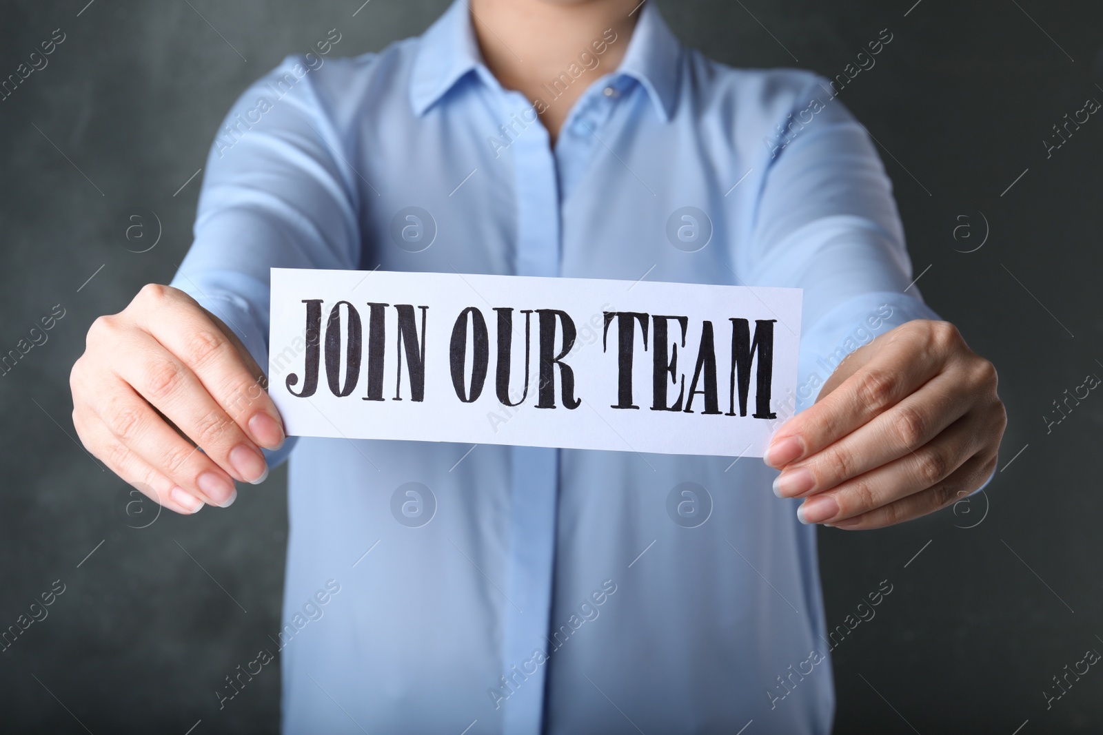 Photo of Woman holding sheet of paper with words JOIN OUR TEAM on grey background, closeup. Career concept