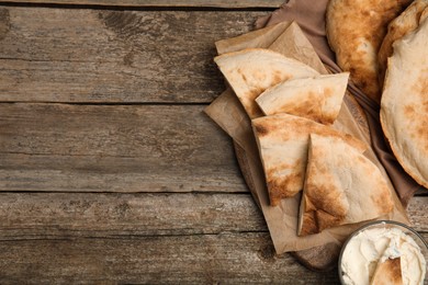 Photo of Pieces of fresh pita bread and cream cheese on wooden table, flat lay. Space for text