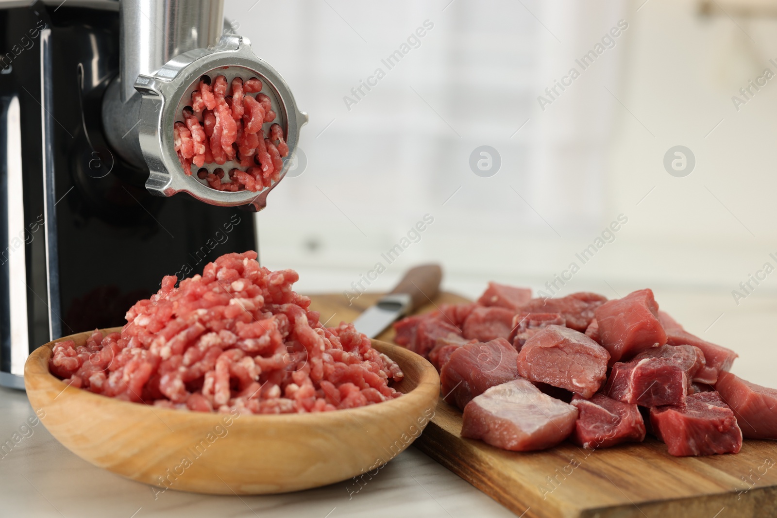 Photo of Electric meat grinder with beef on white table indoors