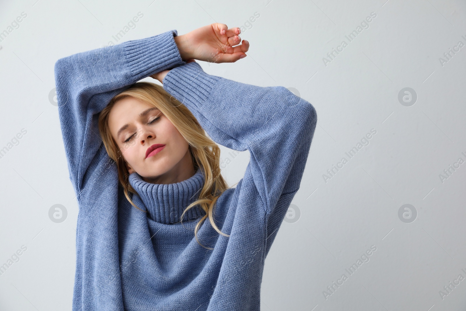 Photo of Beautiful young woman wearing warm blue sweater on light background. Space for text