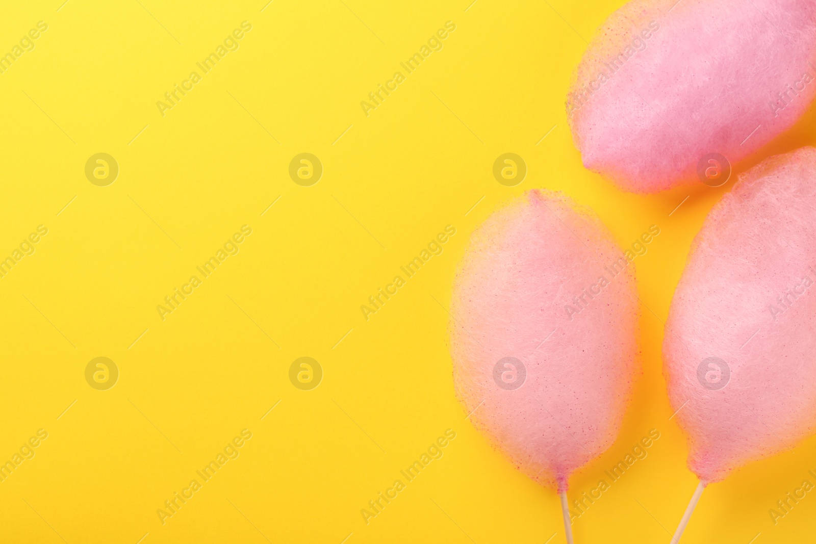 Photo of Sweet pink cotton candies on yellow background, flat lay. Space for text