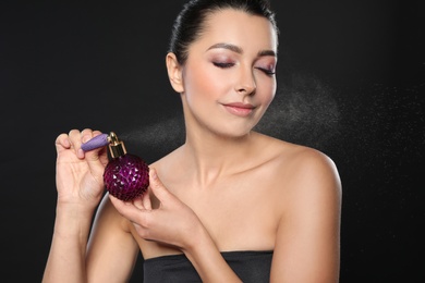 Young woman spraying perfume on black background