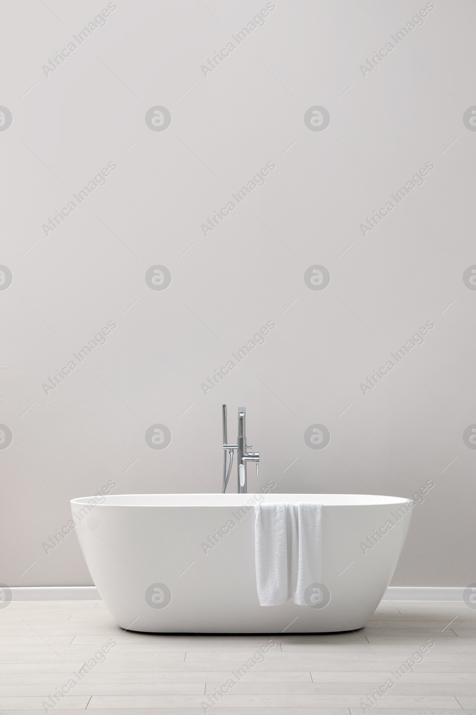 Photo of Modern ceramic bathtub with towel near light wall indoors