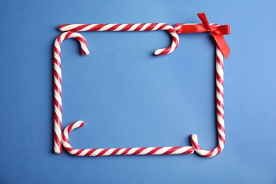 Photo of Frame made of candy canes on blue background, top view. Space for text