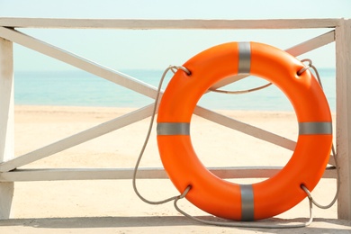 Photo of Orange life buoy near wooden railing on beach.  Emergency rescue equipment