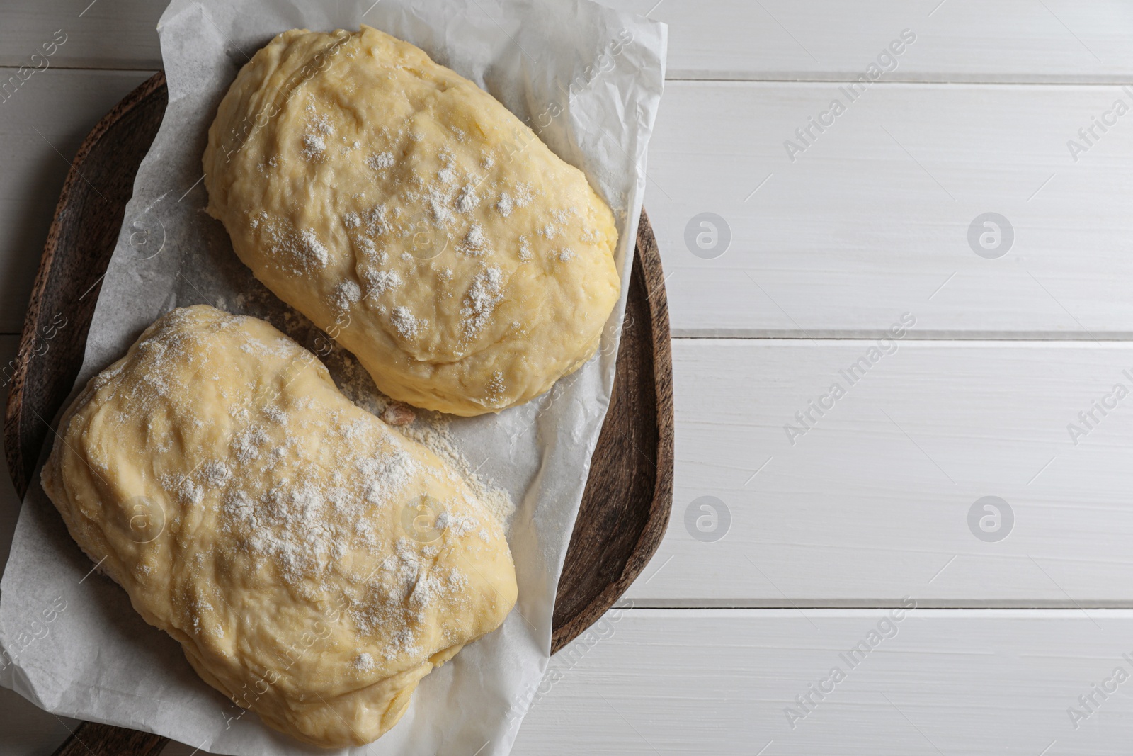 Photo of Raw dough and flour on white wooden table, top view with space for text. Cooking ciabatta