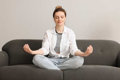 Photo of Woman meditating on sofa near light grey wall. Harmony and zen
