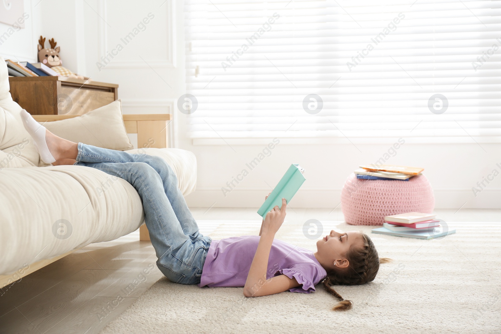 Photo of Cute little girl reading book on floor at home