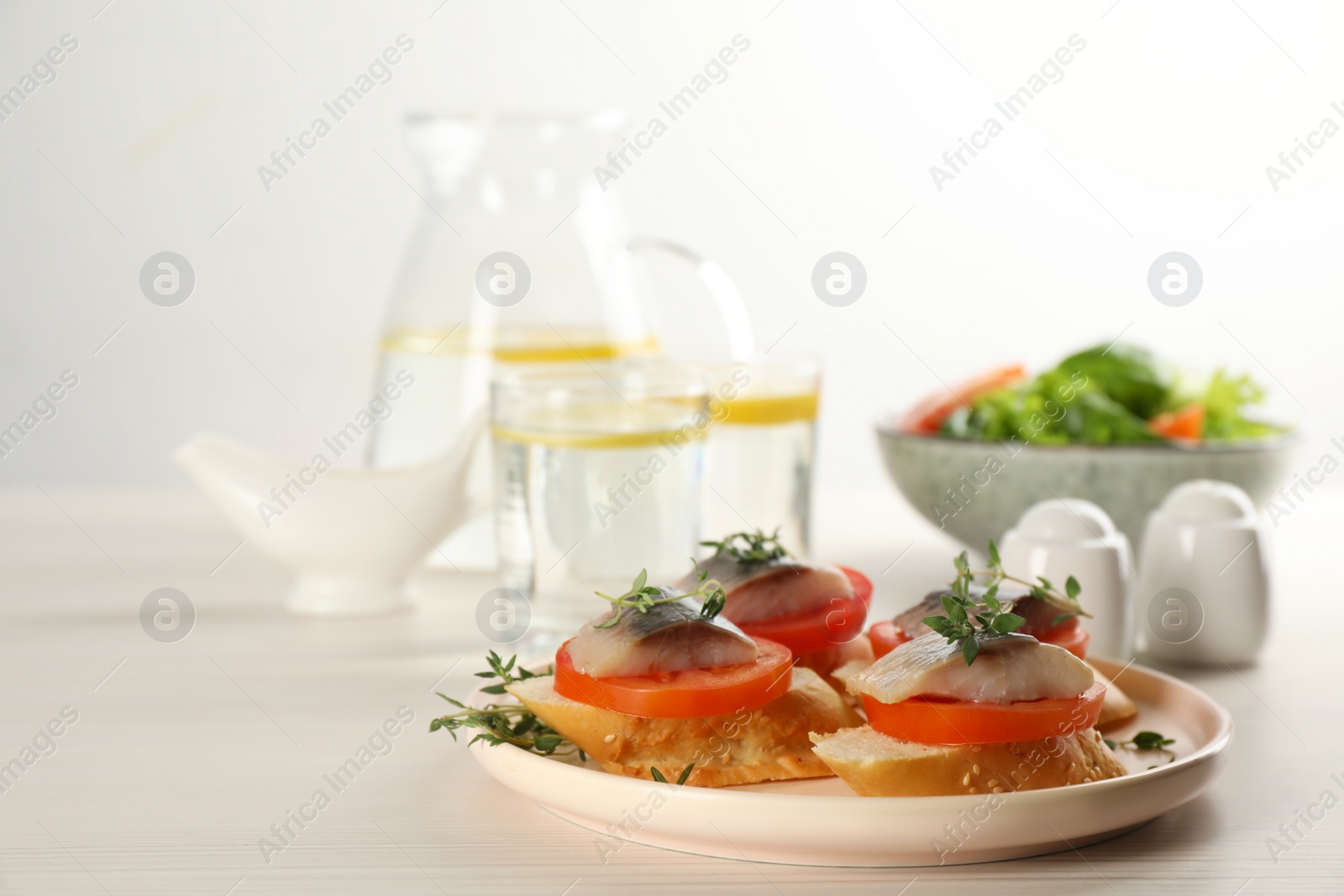 Photo of Delicious sandwiches with salted herring, tomatoes and thyme on light beige wooden table. Space for text