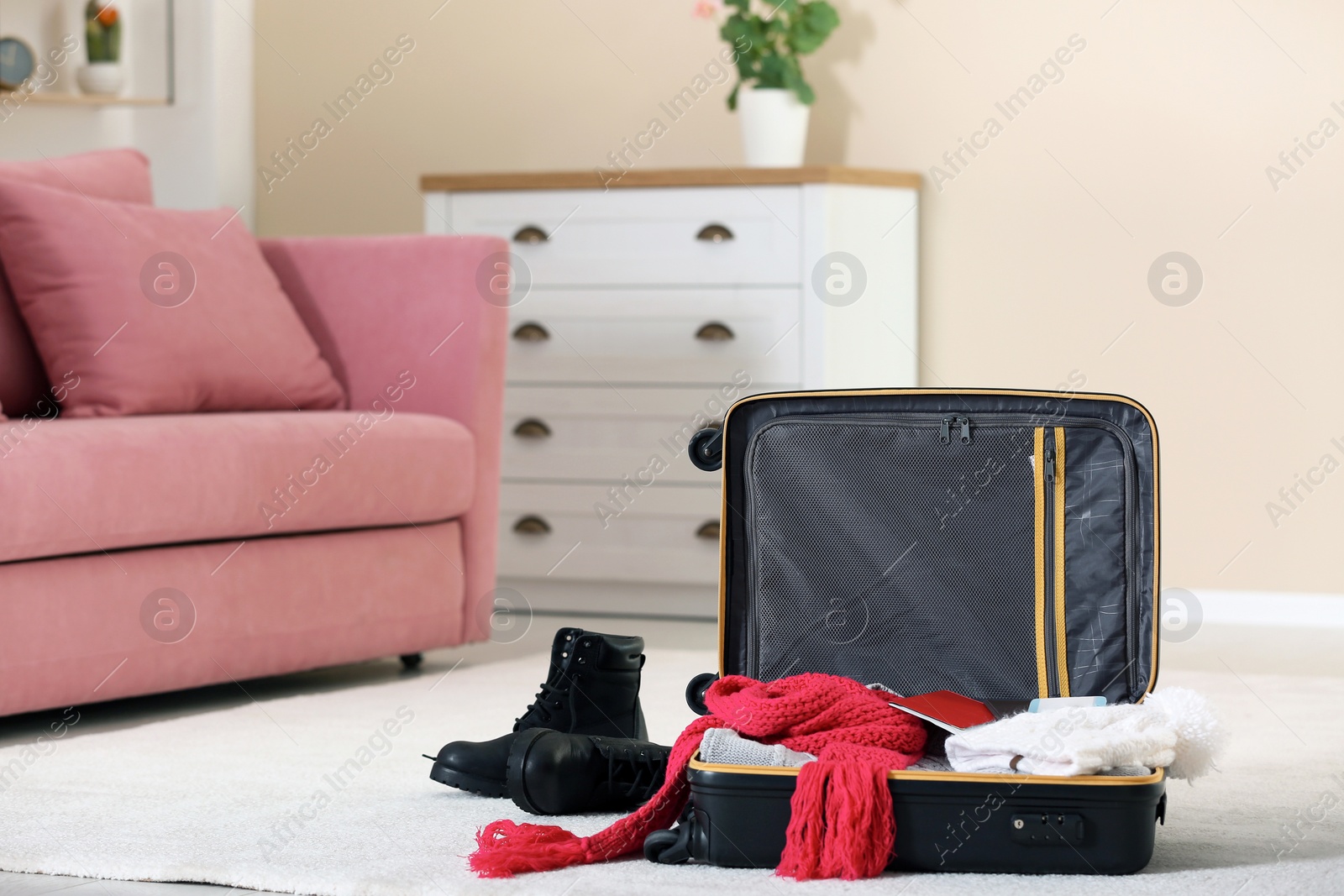 Photo of Modern suitcase with warm clothes on floor indoors. Space for text