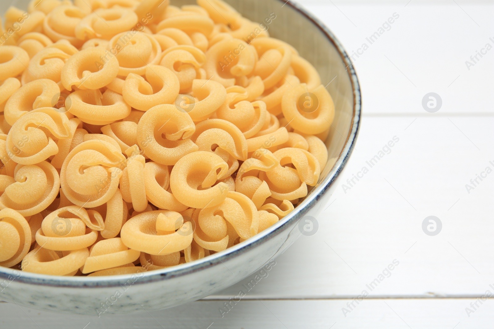 Photo of Raw dischi volanti pasta in bowl on white wooden table, closeup