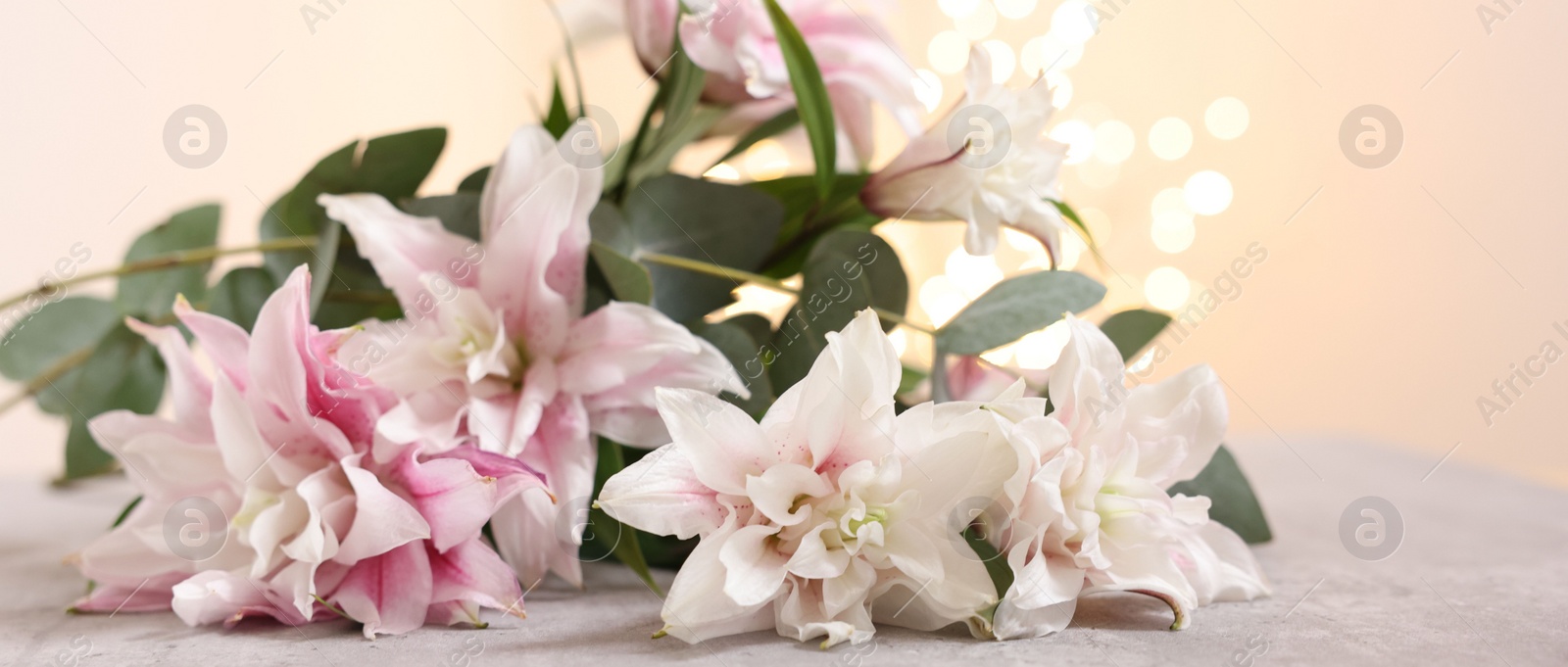 Photo of Bouquet of beautiful lily flowers on table against beige background with blurred lights, closeup