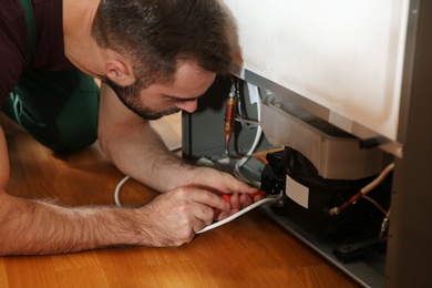 Photo of Male technician in uniform repairing refrigerator indoors