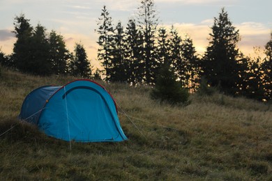 Photo of Blue camping tent on hill near forest, space for text