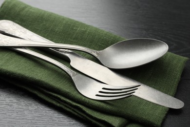 Photo of Stylish setting with cutlery and napkin on black wooden table, closeup