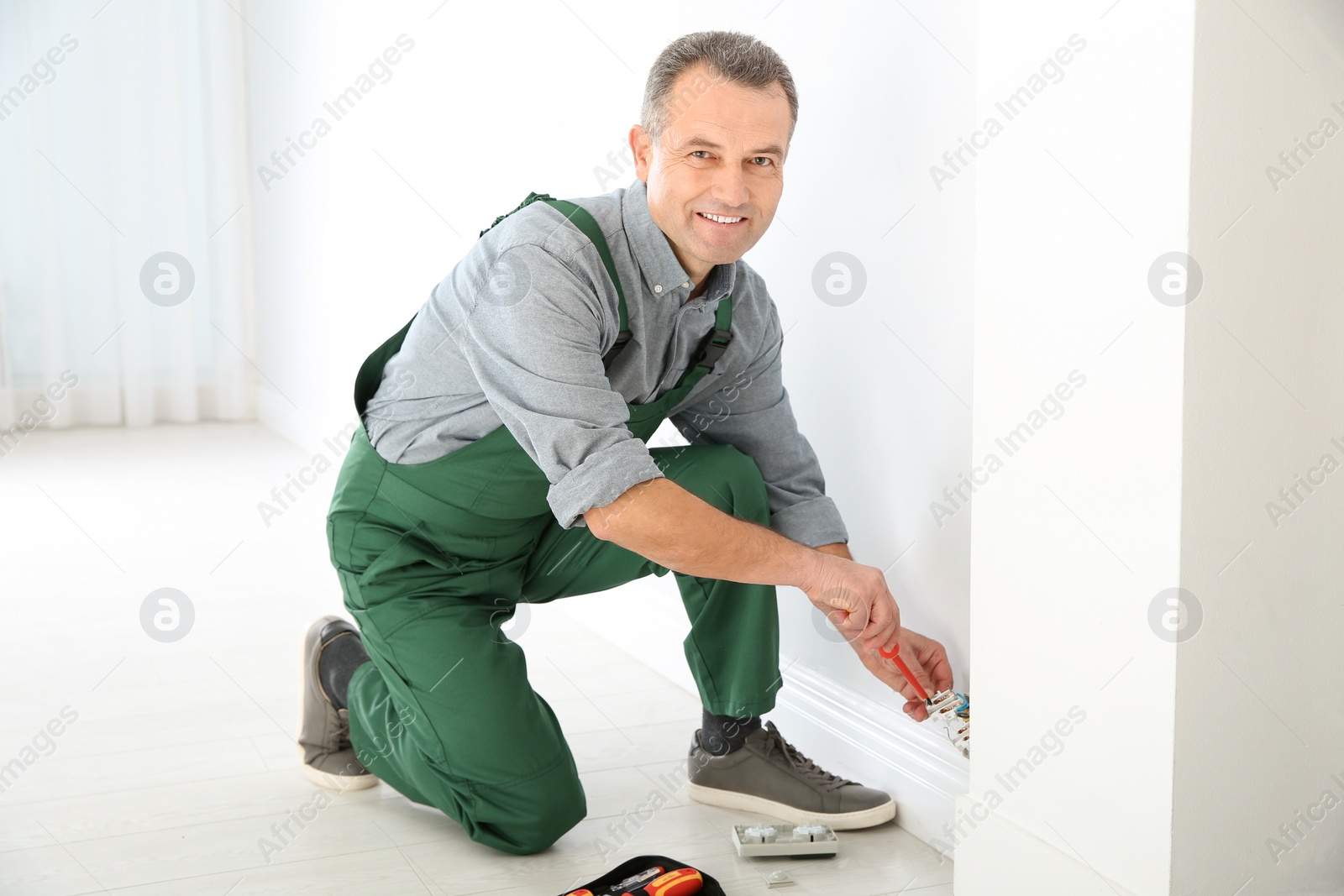 Photo of Electrician with screwdriver repairing power socket indoors