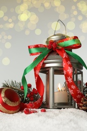 Photo of Decorative lantern and Christmas decor on snow against festive lights