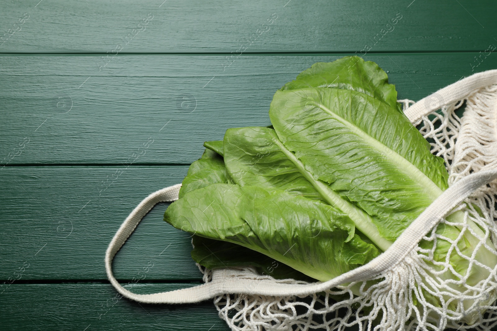 Photo of Net bag with fresh cos lettuce on green wooden table, top view. Space for text