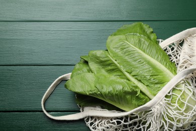 Photo of Net bag with fresh cos lettuce on green wooden table, top view. Space for text