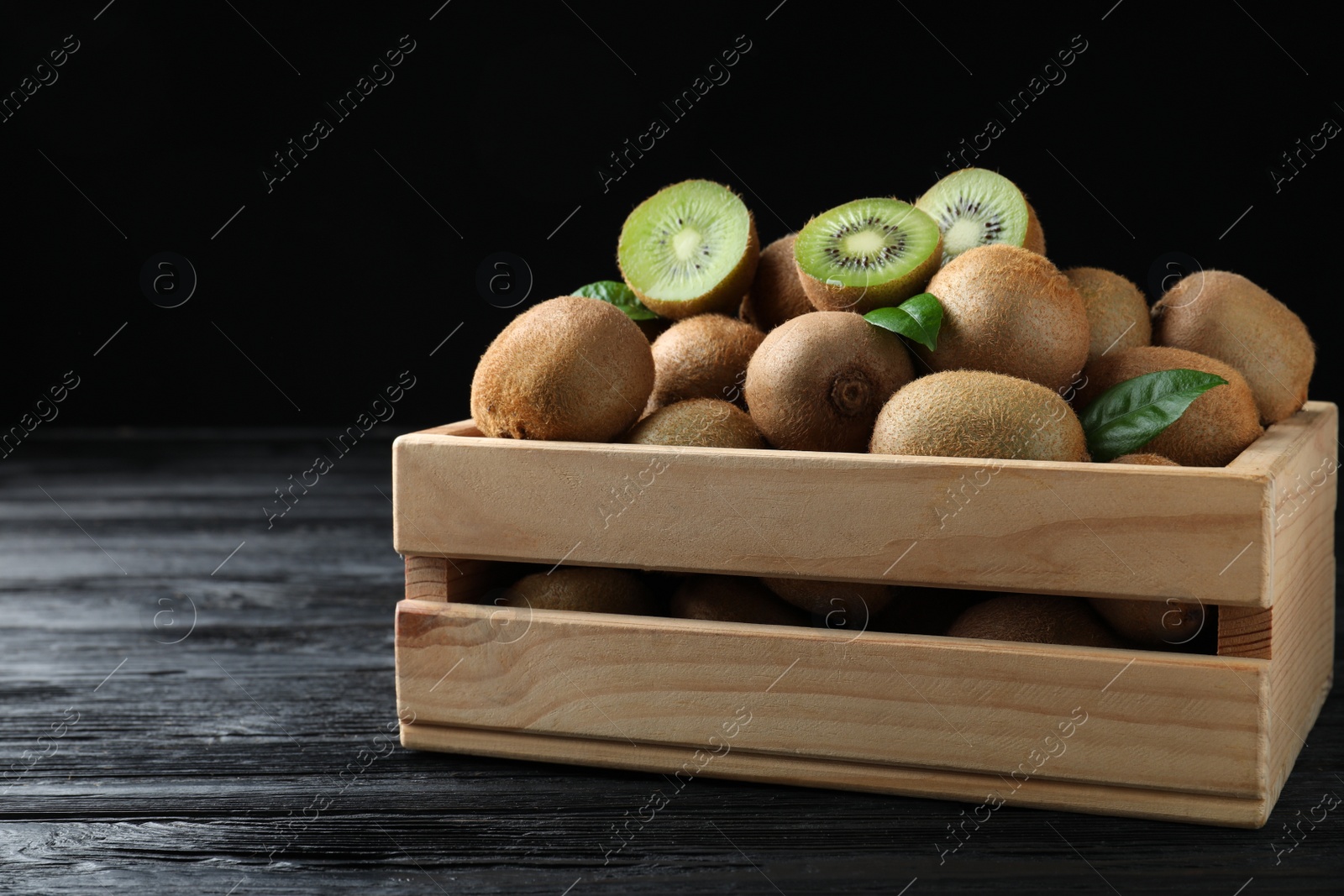 Photo of Crate with cut and whole fresh kiwis on black wooden table