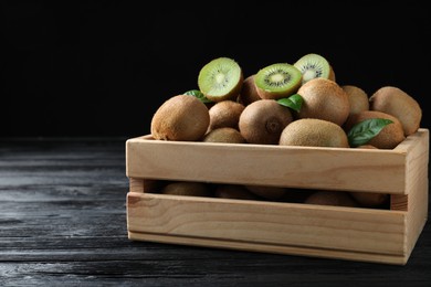 Photo of Crate with cut and whole fresh kiwis on black wooden table