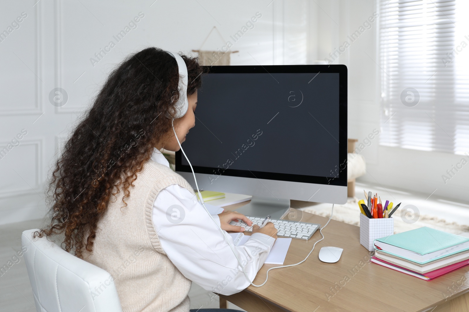 Photo of African American woman with headphones using modern computer for studying at home. Distance learning