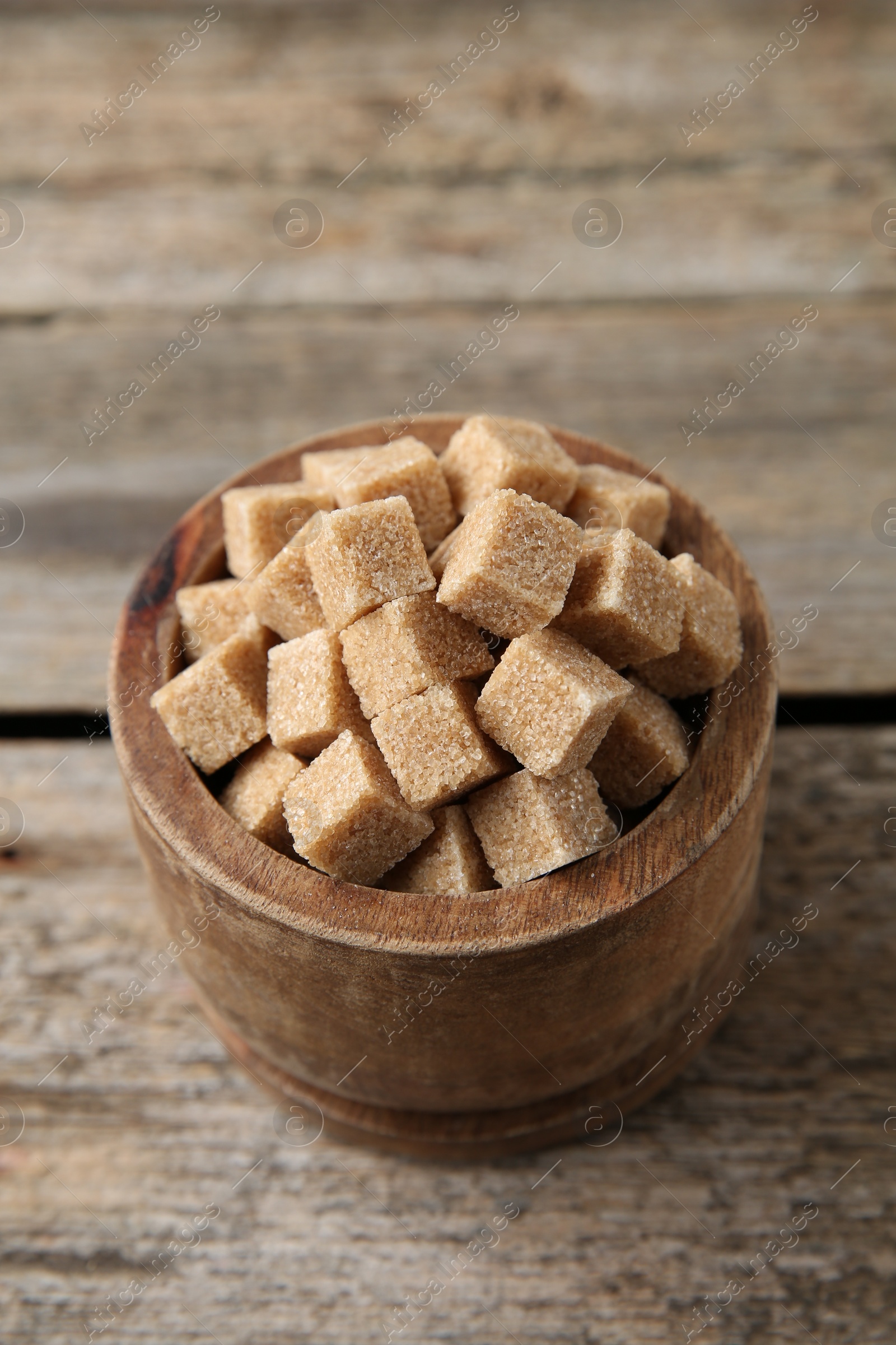 Photo of Brown sugar cubes in bowl on wooden table, closeup