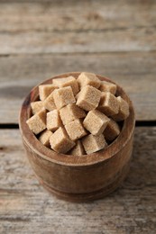 Photo of Brown sugar cubes in bowl on wooden table, closeup