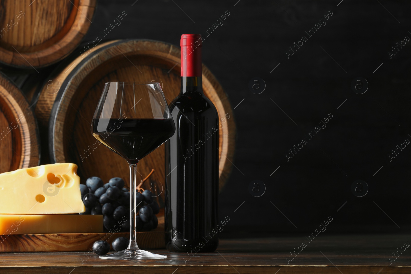 Photo of Delicious wine, wooden barrels, cheese and fresh grapes on table, space for text