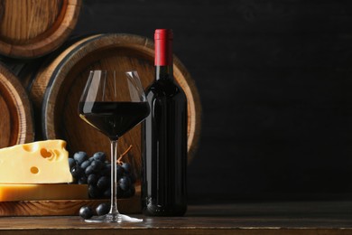 Delicious wine, wooden barrels, cheese and fresh grapes on table, space for text